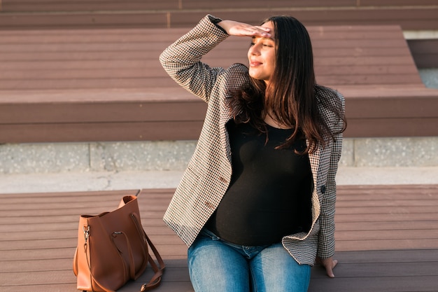 Concetto di gravidanza attiva. Felice giovane impresa o studente donna incinta seduta sulla panchina. Futura mamma che lavora o studia durante il suo periodo di gravidanza avanzata.