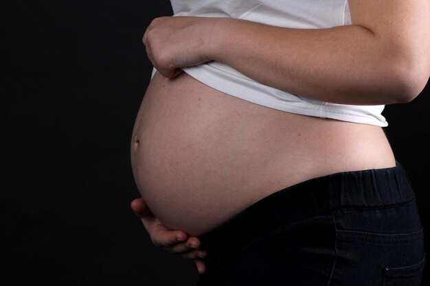 Concetto di gravidanza del ventre della donna incinta isolato su sfondo nero Pancia incinta da vicino