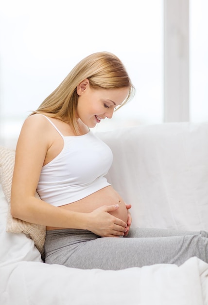 concetto di gravidanza, maternità e felicità - donna incinta felice che si siede sul divano e si tocca la pancia