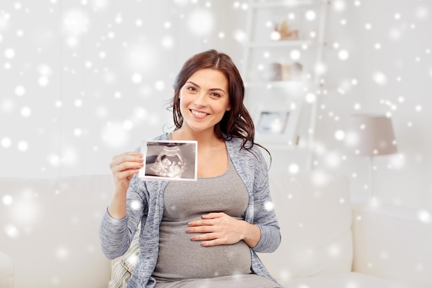 concetto di gravidanza, maternità, persone, inverno e medicina - donna incinta felice che tiene l'immagine ecografica a casa sopra la neve