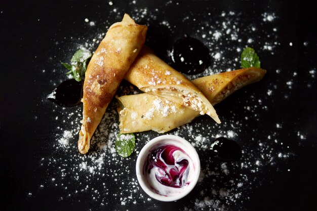 Concetto di gustosa colazione estiva sana. Frittelle di ricotta con menta fresca su un piatto nero cosparso di zucchero a velo.