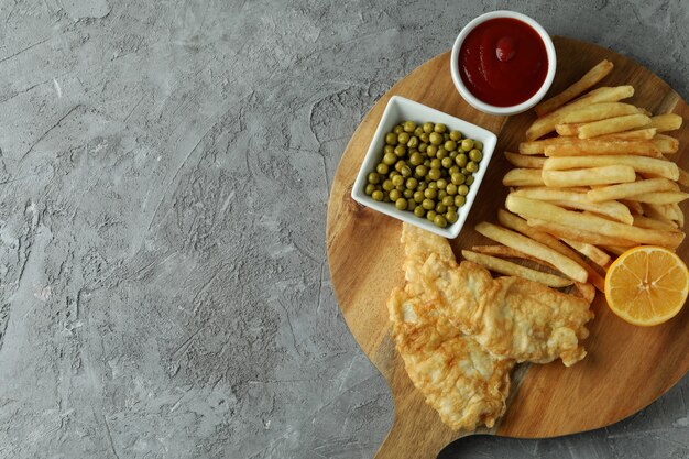 Concetto di gustoso mangiare con pesce fritto e patatine fritte su grigio testurizzato