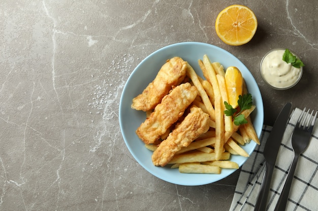 Concetto di gustoso mangiare con pesce fritto e patatine fritte sulla tabella strutturata grigia