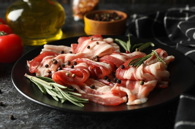 Concetto di gustoso spuntino con piatto di pancetta sulla superficie nera affumicata