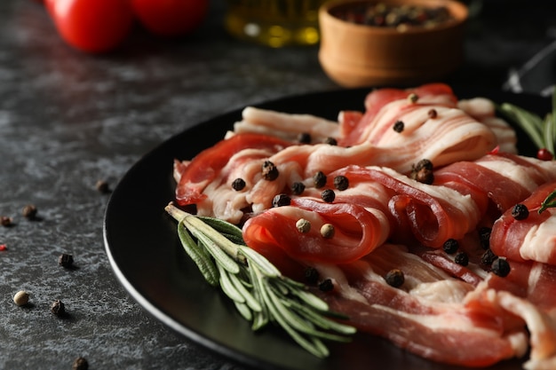 Concetto di gustoso spuntino con piatto di pancetta sulla superficie nera affumicata