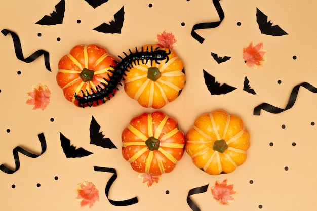 Concetto di Halloween Centipede su zucche dal sorriso spaventoso e fantasma con pipistrello nero su sfondo crema