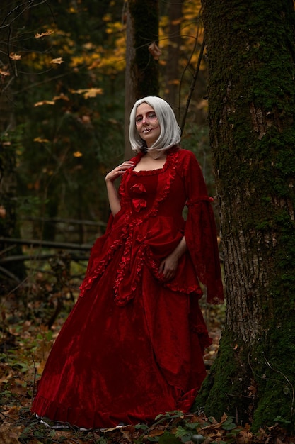 Concetto di Halloween, dettaglio glamour del costume. Giovane bella e misteriosa donna nei boschi, in abito bianco e mantello rosso. Cappuccetto rosso o storia di vampiri.