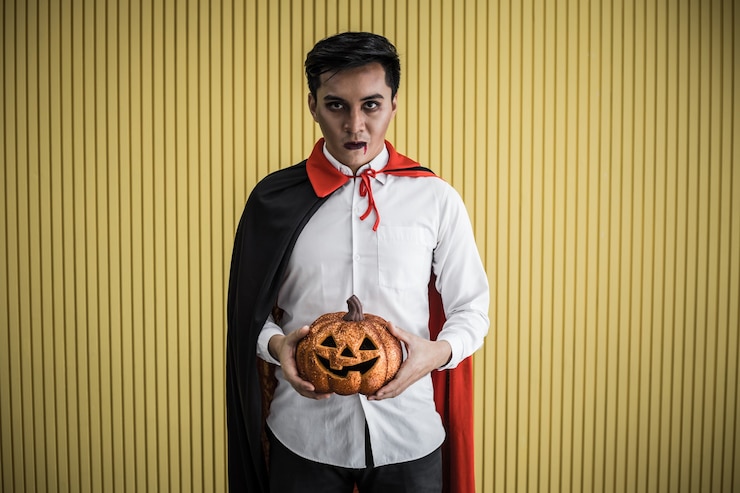 Foto concetto di halloween di giovane uomo asiatico in costume dracula e tenere la zucca arancione di halloween su sfondo giallo. ritratto di uomo adolescente vestito da dracula per celebrare il festival di halloween.