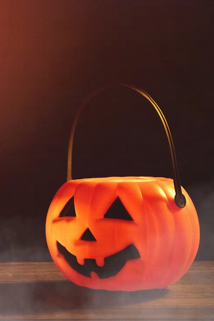 Concetto di Halloween - Lanterna di zucca in plastica arancione su un tavolo di legno scuro con luce scintillante sfocata sullo sfondo, dolcetto o scherzetto, primo piano