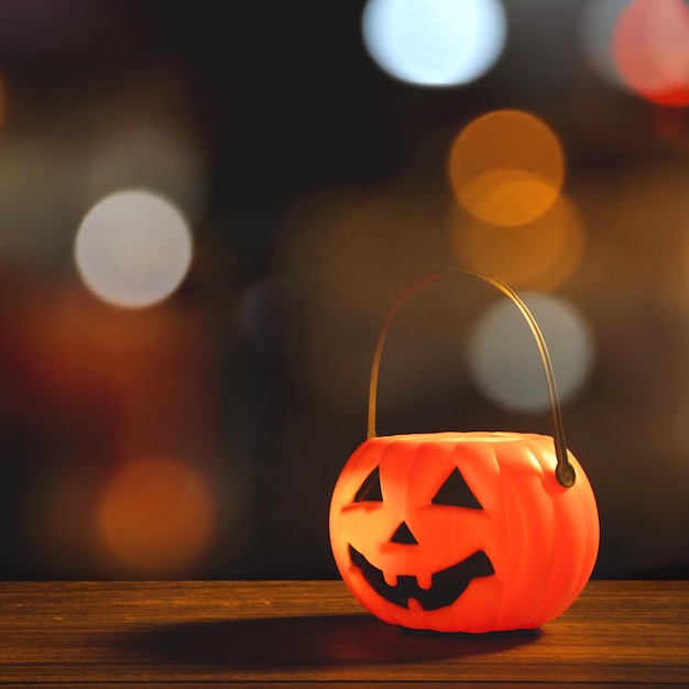 Concetto di Halloween Lanterna di zucca in plastica arancione su un tavolo di legno scuro con una luce scintillante sfocata sullo sfondo Dolcetto o scherzetto da vicino