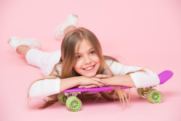 Concetto di hobby per adolescenti Alla ragazza piace andare in skateboard e stile di vita sportivo Ragazza sul viso sorridente in posa con penny board sfondo rosa Kid ragazza con i capelli lunghi pronta a guidare penny board