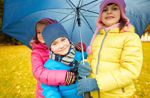 concetto di infanzia, amicizia, stagione, tempo e persone - gruppo di bambini felici con ombrellone nel parco autunnale