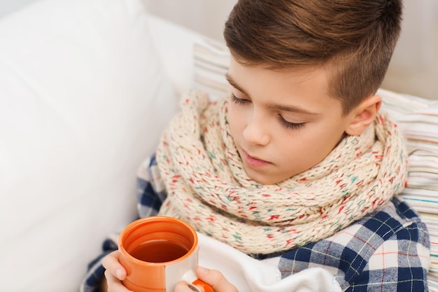 concetto di infanzia, assistenza sanitaria, persone e medicina - ragazzo malato con influenza sdraiato a letto e bevendo tè a casa