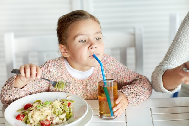 concetto di infanzia, cibo e persone - bambina che mangia pasta e beve succo di mela per cena al ristorante o al bar