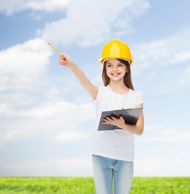 concetto di infanzia, costruzione, architettura, costruzione e persone - bambina sorridente in casco protettivo con appunti a matita