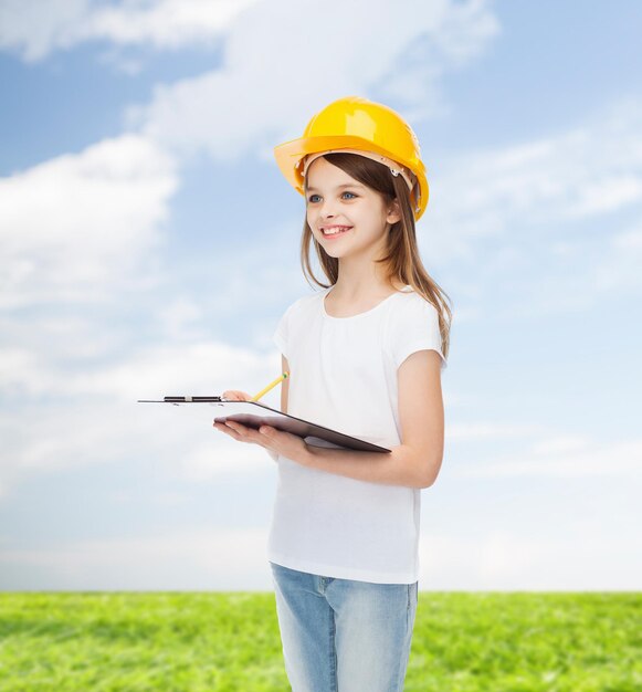 concetto di infanzia, costruzione, architettura, costruzione e persone - bambina sorridente in casco protettivo con appunti che prendono appunti