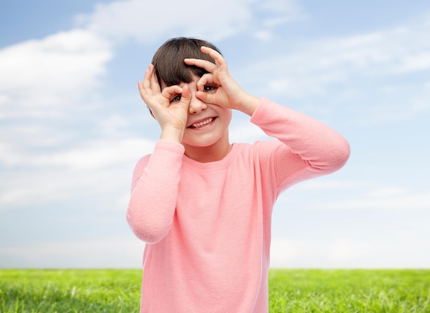 concetto di infanzia, divertimento, gesto e persone - bambina felice che fa le facce sopra il cielo blu e lo sfondo dell'erba