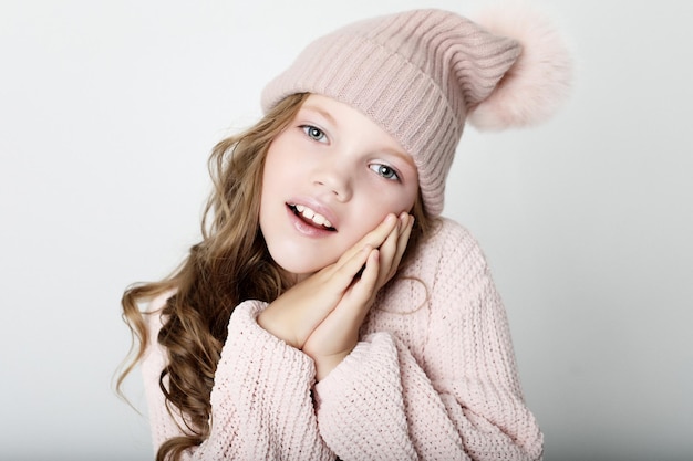 Concetto di infanzia e moda della gente bambina che indossa un cappello invernale rosa e un maglione su sfondo rosa