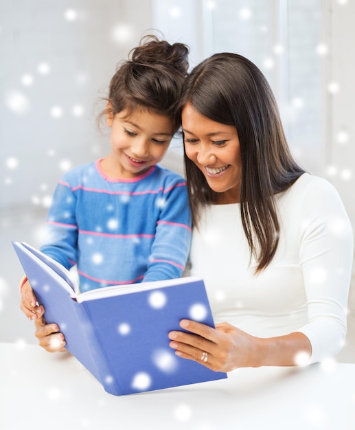 concetto di infanzia, educazione, famiglia e persone - bambina sorridente e madre o insegnante con libro all'interno