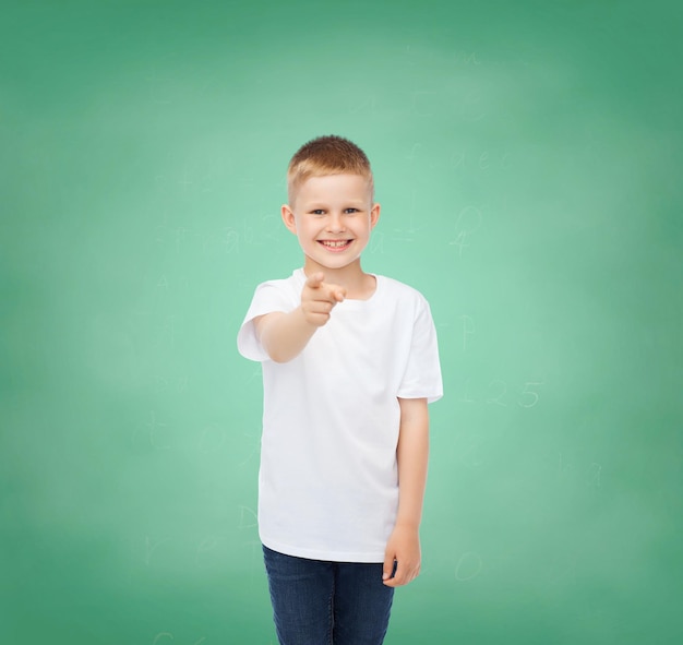 concetto di infanzia, gesto, istruzione e pubblicità - ragazzo sorridente in maglietta bianca che punta il dito su di te su sfondo verde