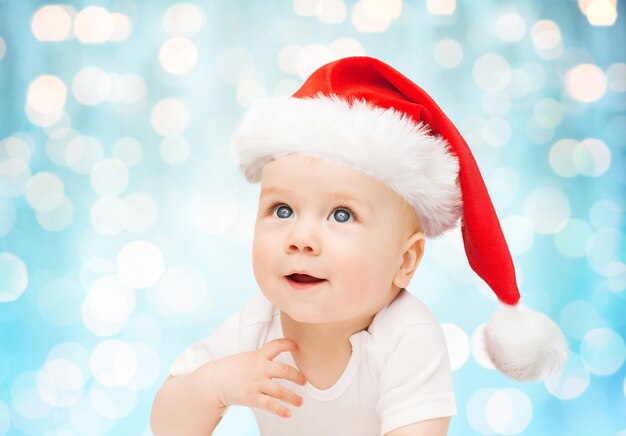 concetto di infanzia, natale, vacanze e persone - bellissimo bambino piccolo in cappello di babbo natale su sfondo di luci blu