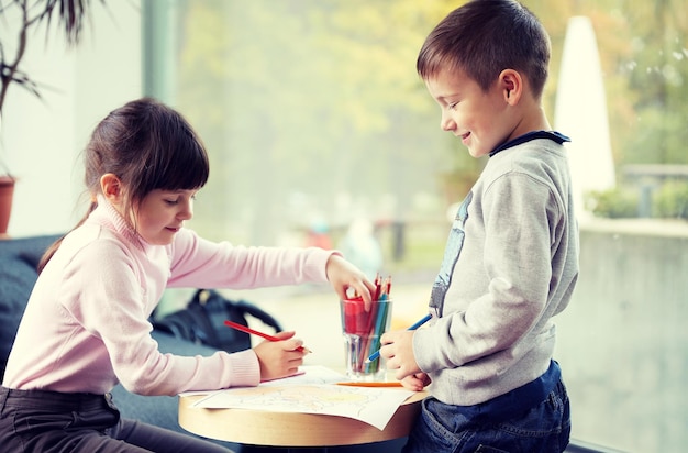 concetto di infanzia, tempo libero, amicizia e persone - bambina felice e ragazzo che disegnano e colorano l'immagine con le matite a casa