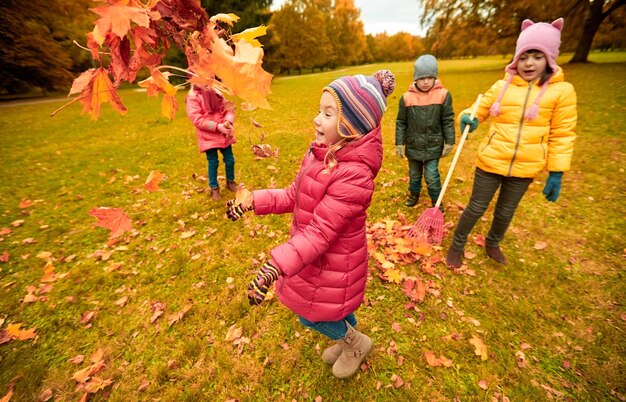 concetto di infanzia, tempo libero, amicizia e persone - gruppo di bambini felici che giocano con e travasano foglie d'acero autunnali e si divertono nel parco