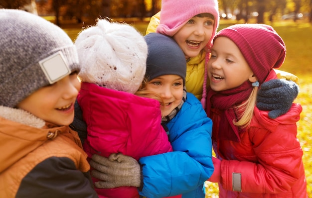 concetto di infanzia, tempo libero, amicizia e persone - gruppo di bambini felici che si abbracciano nel parco autunnale