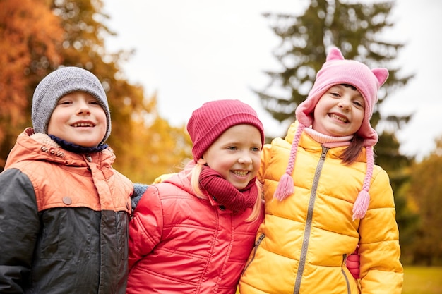 concetto di infanzia, tempo libero, amicizia e persone - gruppo di bambini felici che si abbracciano nel parco autunnale