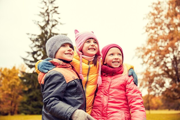 concetto di infanzia, tempo libero, amicizia e persone - gruppo di bambini felici che si abbracciano nel parco autunnale