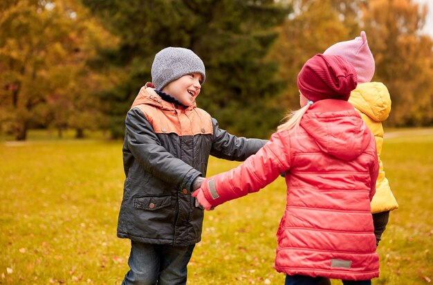 concetto di infanzia, tempo libero, amicizia e persone - gruppo di bambini felici che si tengono per mano e giocano nel parco autunnale