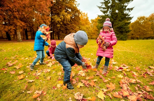 concetto di infanzia, tempo libero, autunno, amicizia e persone - gruppo di bambini che raccolgono foglie nel parco