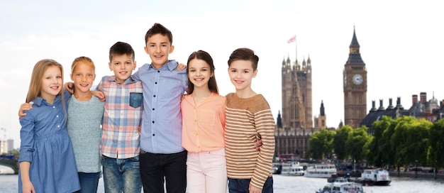 concetto di infanzia, viaggio, turismo, amicizia e persone - bambini sorridenti felici che si abbracciano sullo sfondo della città di londra