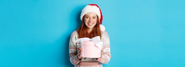 Concetto di inverno e celebrazione adorabile ragazza rossa che ti regala un regalo augurando buon natale st