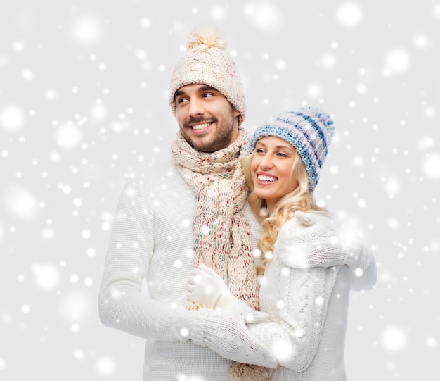 concetto di inverno, moda, coppia, natale e persone - uomo e donna sorridenti in cappelli e avvolgenti sciarpe