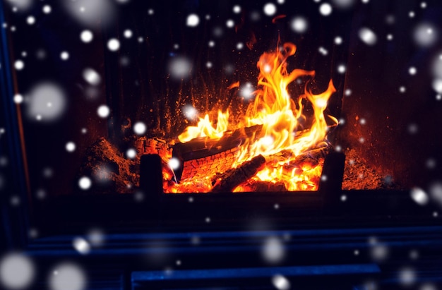 concetto di inverno, natale, calore, fuoco e intimità - primo piano del caminetto acceso con la neve