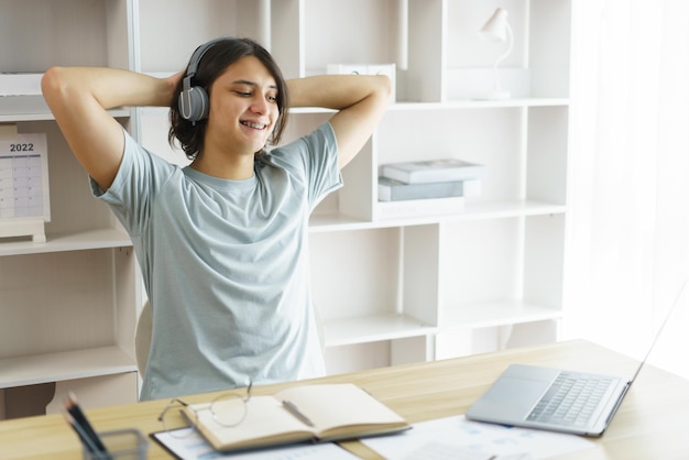 Concetto di istruzione a distanza Il ragazzo adolescente ascolta musica e si allunga per rilassarsi dopo aver studiato duramente online