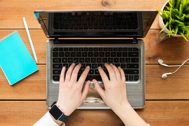 concetto di istruzione, affari, persone e tecnologia - primo piano di donna o studente che digita su computer portatile con notebook e auricolari su tavolo di legno