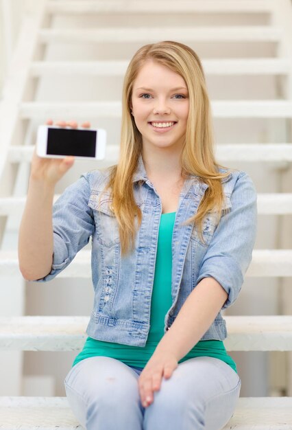concetto di istruzione e tecnologia - studentessa sorridente che mostra lo schermo vuoto dello smartphone seduto sulla scala