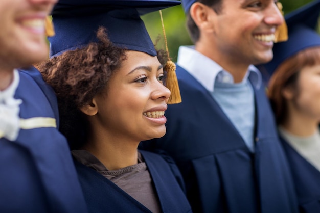 concetto di istruzione, laurea e persone - gruppo di studenti internazionali felici in tavole di mortaio e abiti da scapolo all'aperto