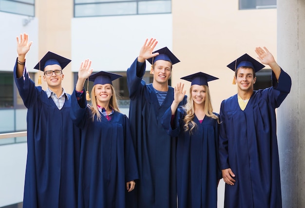 concetto di istruzione, laurea e persone - gruppo di studenti sorridenti in sparvieri e abiti che agitano le mani all'aperto