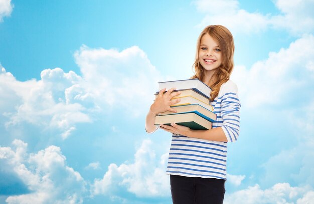 concetto di istruzione, persone, bambini e scuola - ragazza studentessa felice con molti libri sopra il cielo blu con sfondo di nuvole