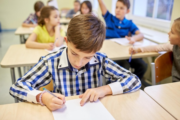 concetto di istruzione, scuola elementare, apprendimento e persone - gruppo di bambini in età scolare con penne e quaderni che scrivono test in classe