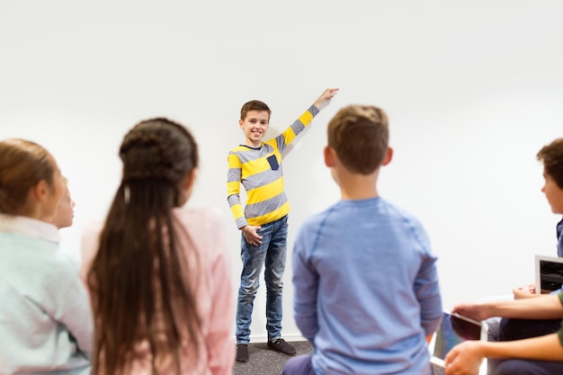 concetto di istruzione, scuola elementare, apprendimento e persone - ragazzo studente felice che mostra qualcosa al muro bianco