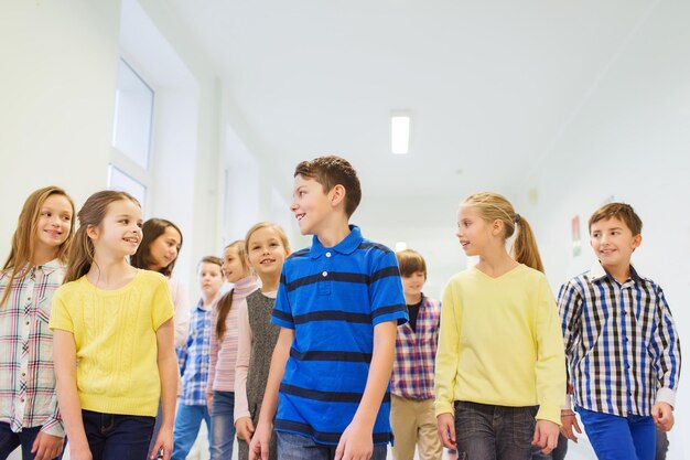 concetto di istruzione, scuola elementare, bevande, bambini e persone - gruppo di scolari sorridenti che camminano nel corridoio