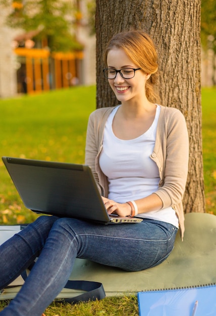 concetto di istruzione, tecnologia e internet - adolescente sorridente in occhiali con computer portatile e notebook