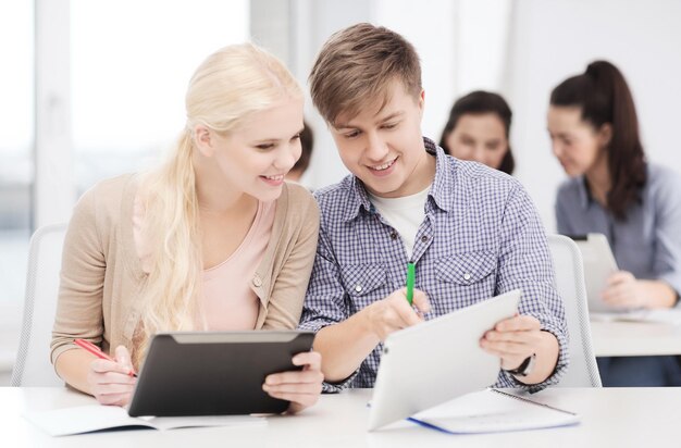 concetto di istruzione, tecnologia e internet - due studenti sorridenti con tablet pc e notebook a scuola