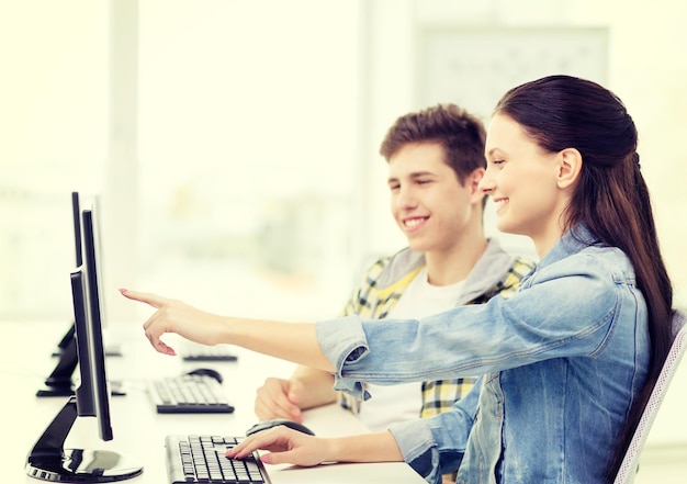 concetto di istruzione, tecnologia e scuola - due studenti sorridenti in classe di computer, ragazza che punta il dito sullo schermo