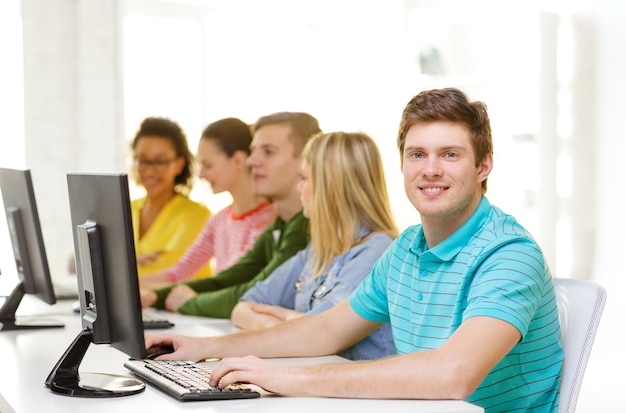 concetto di istruzione, tecnologia e scuola - studente maschio sorridente con i compagni di classe in classe di computer