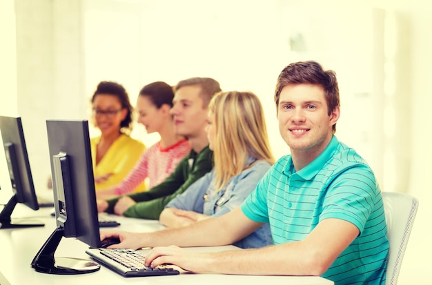 concetto di istruzione, tecnologia e scuola - studente maschio sorridente con i compagni di classe in classe di computer